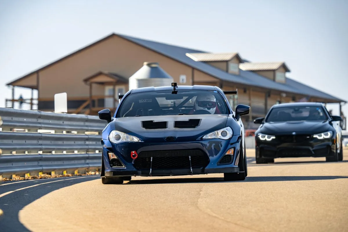 Dark blue Toyota GT86 with a front splitter leading a BMW out of a corner
