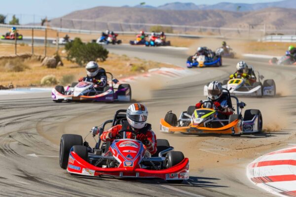 A group of go-karts race around a desert track, the leading kart in focus.